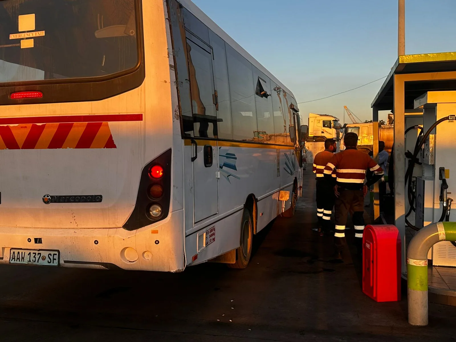 Autocarro numa área de abastecimento, com trabalhadores junto às bombas de combustível