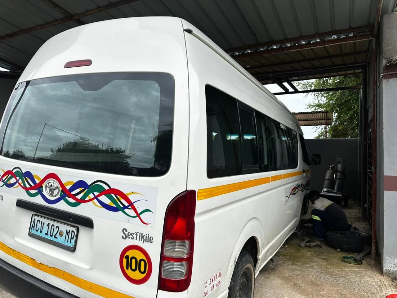 Miniautocarro numa oficina, com uma pessoa junto à roda traseira